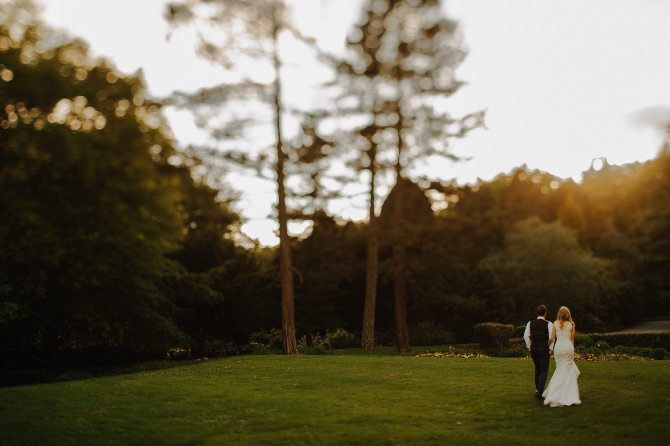 Die Braut und der Bräutigam gehen auf grünem Gras in Richtung der Bäume im Hintergrund.