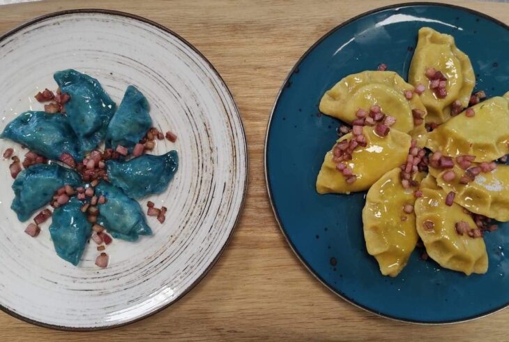 Po lewej biały talerz z niebieskimi pierogami. Po prawej niebieski talerz z żółtymi pierogami.
